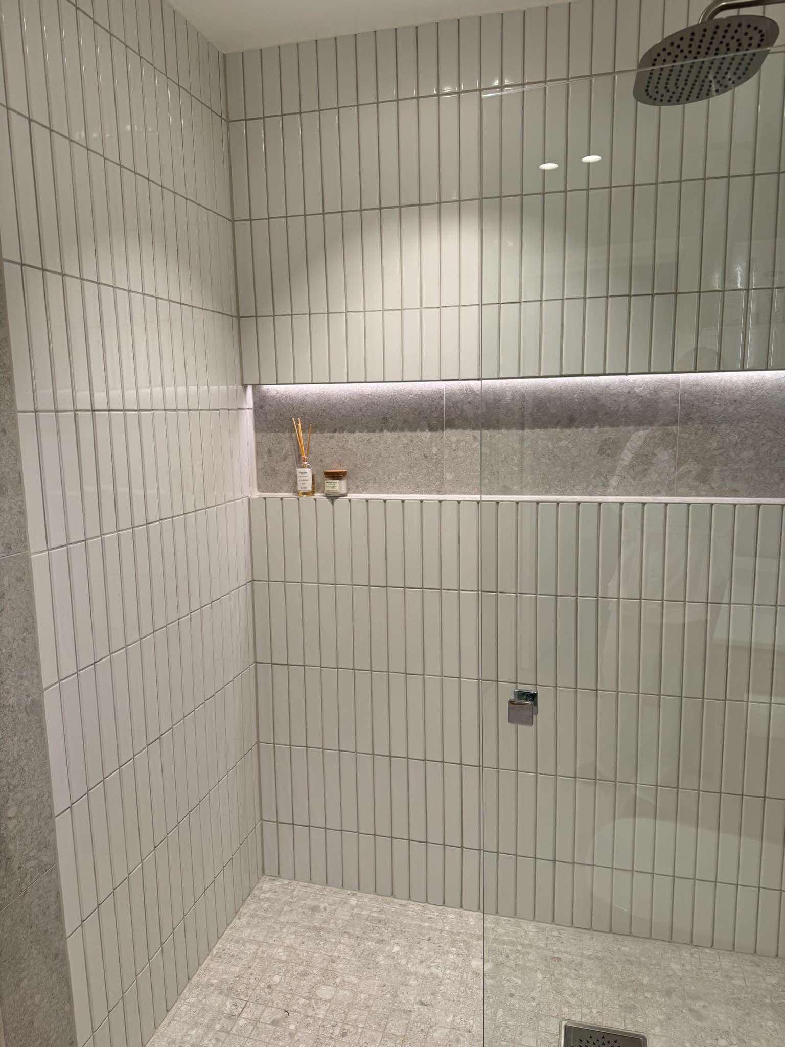 Hvit flis i stående format med innfelt hylle i dusjen